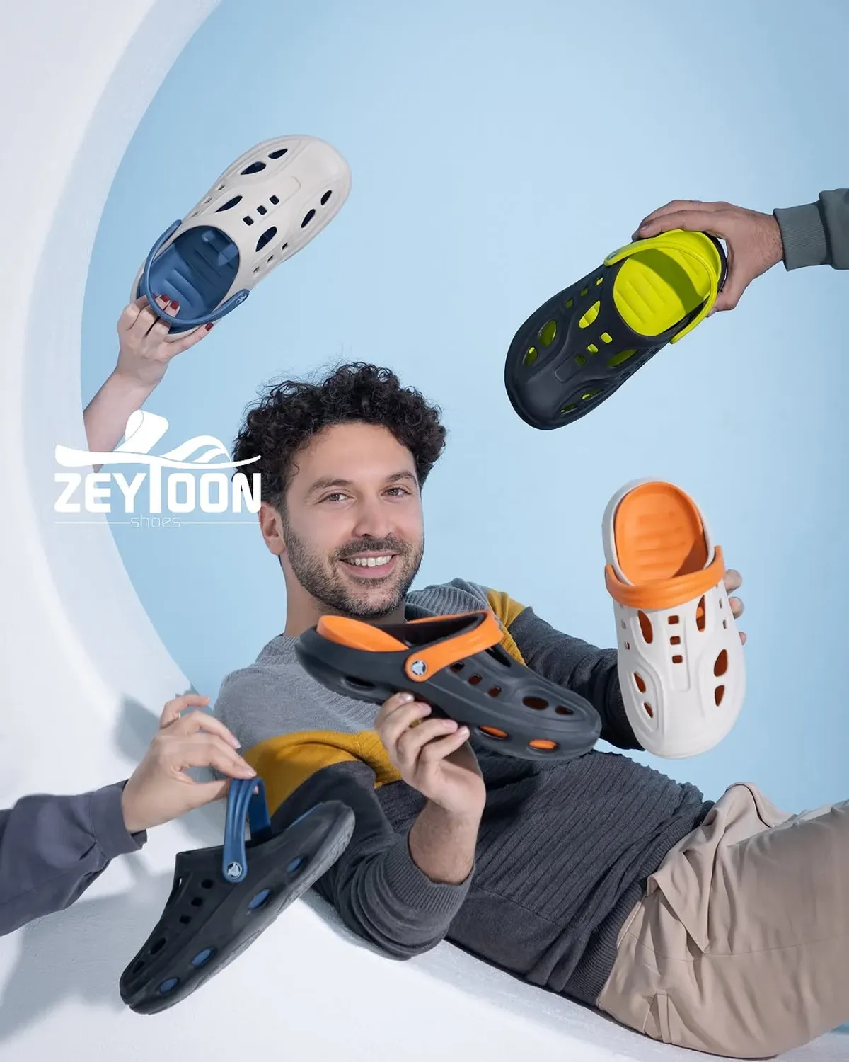 Bir adam iki Crocs terlik tutuyor, dış çerçevede birkaç kişi de Crocs terliklerini tutuyor.