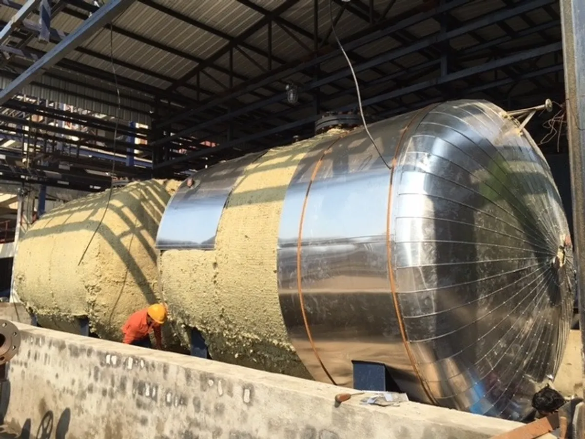 工业现场圆柱形储罐绝热工艺特写；身穿安全服的专家正在罐体上进行热绝热施工并安装钢制覆层，适用于工业保温和减少能量损失。