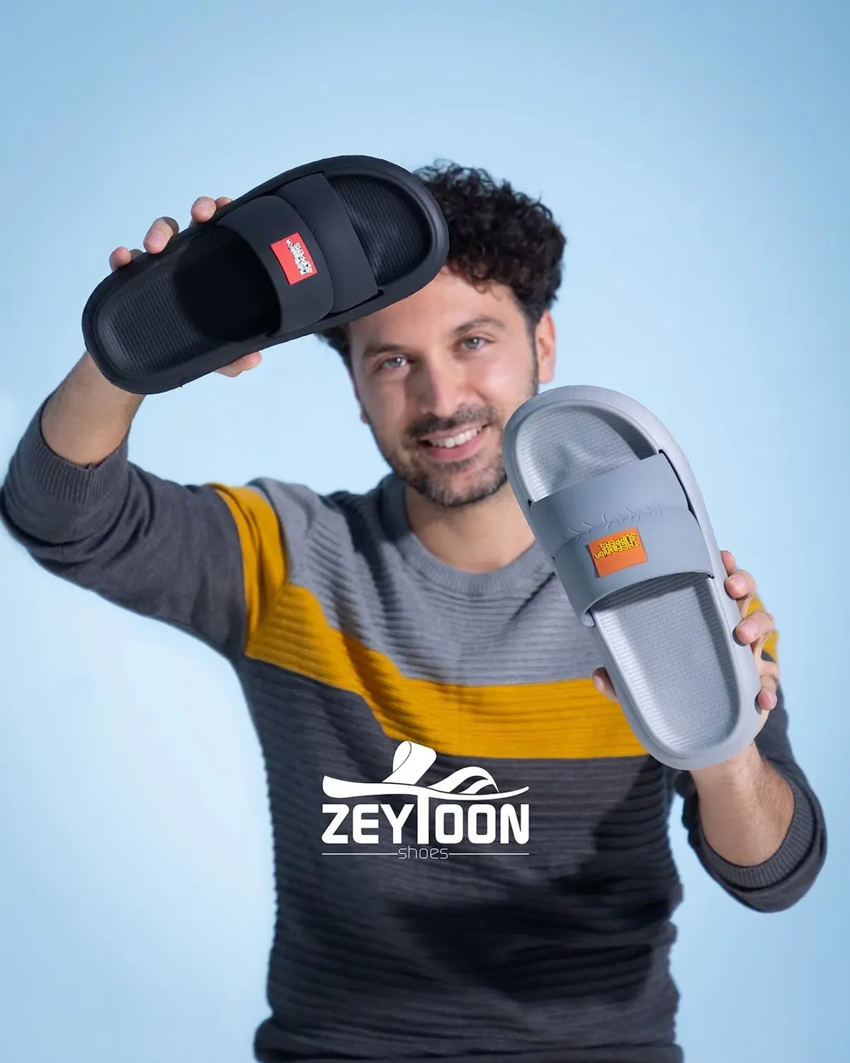 Eliyle terlik tutan ve kameraya bakan bir adam.