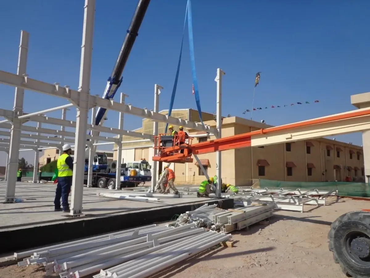 沙漠施工现场的金属结构安装与组装，配有起重机和升降机，纳瓦公司的工人和工程师正按照安全和工程标准搭建厂房/工业建筑的钢骨架。