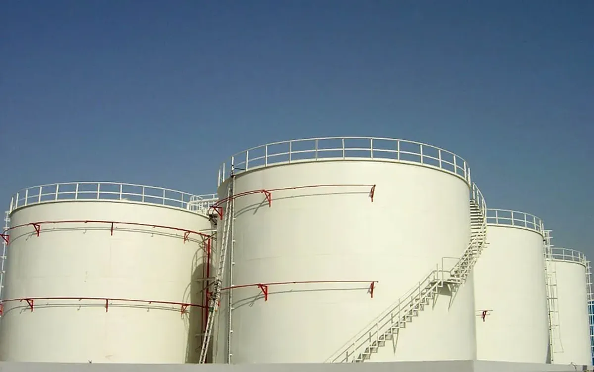 晴空下工业现场几个带安全栏杆和检修梯的大型金属圆柱形储罐特写；适用于储存石油、柴油或化学品。