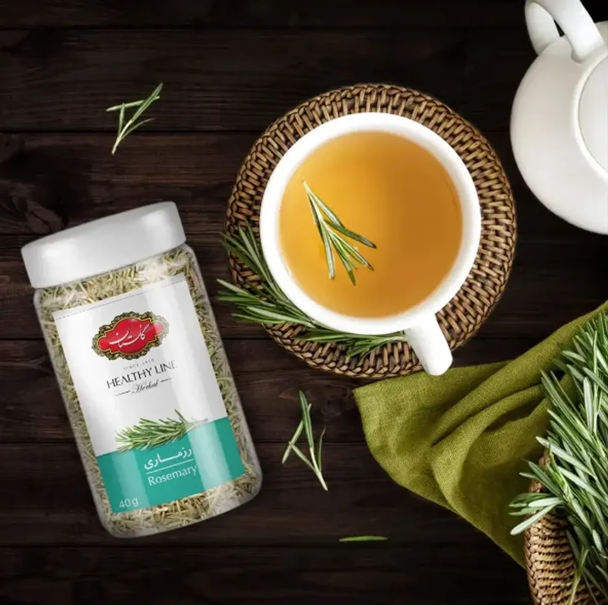 دمنوش رزماری گلستان در فنجان سفید در کنار بسته رزماری خشک و شاخه‌های تازه رزماری