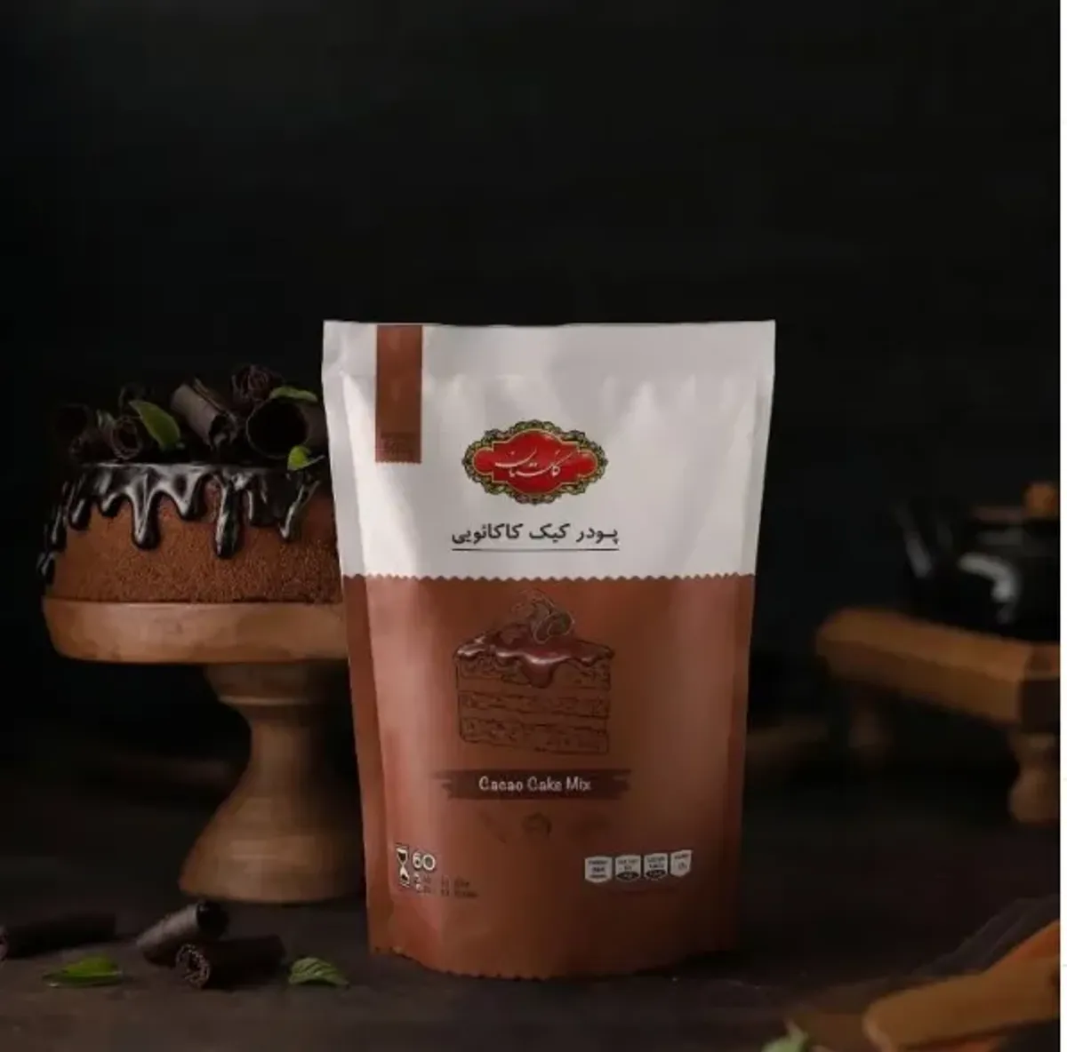 بسته پودر کیک کاکائویی گلستان در کنار کیک شکلاتی با تزئین کاکائو